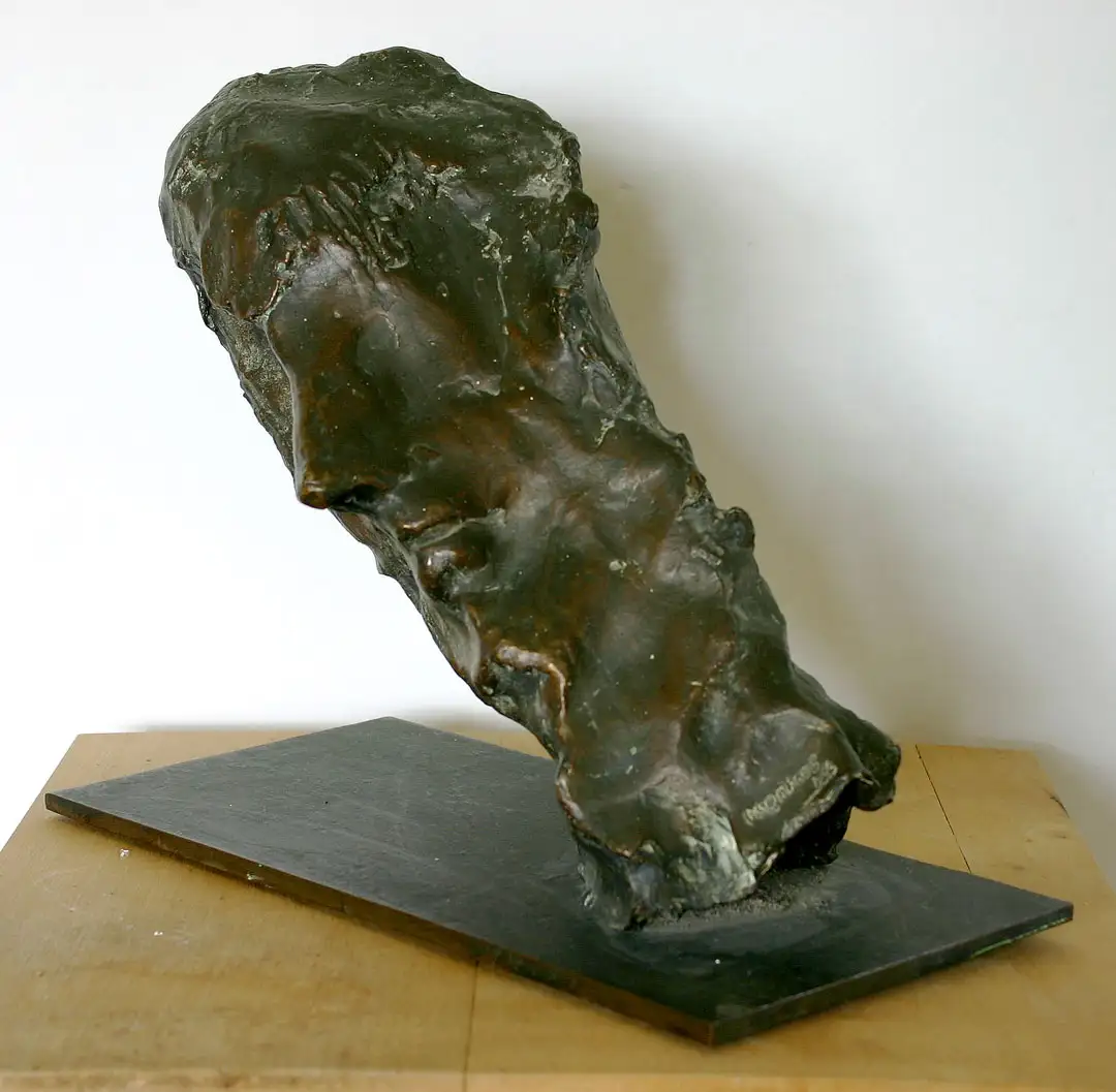 A bronze sculpture of a head, attached at an angle of 45 degrees to a flat base