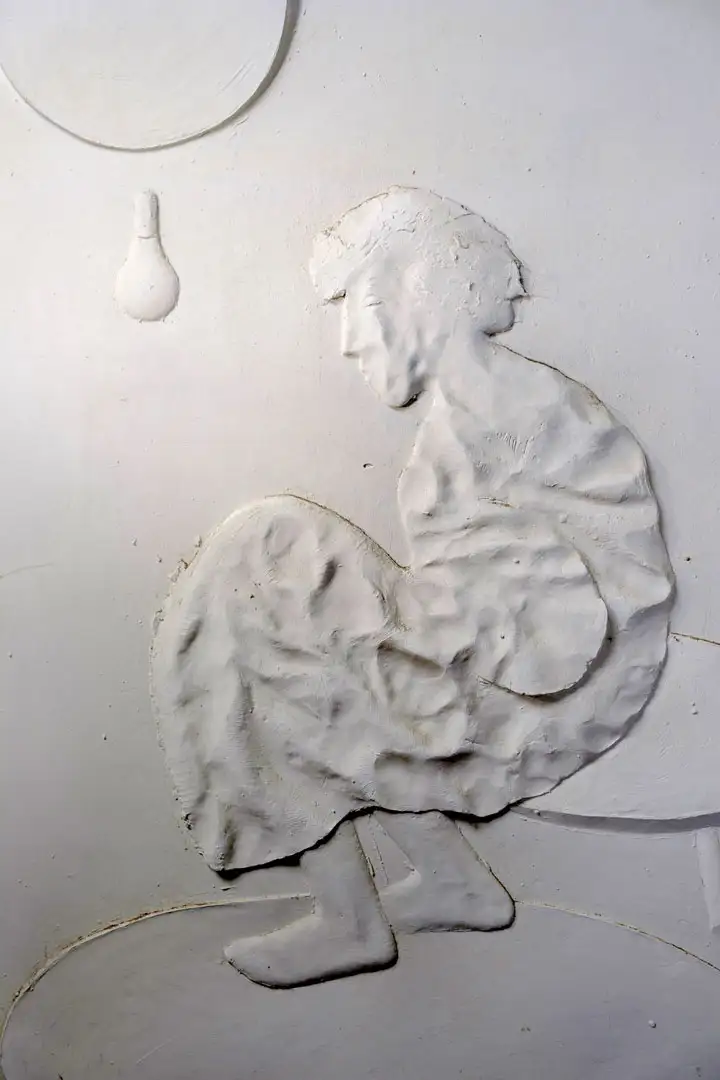 A seated figure facing a bare lightbulb, relief cast in resin