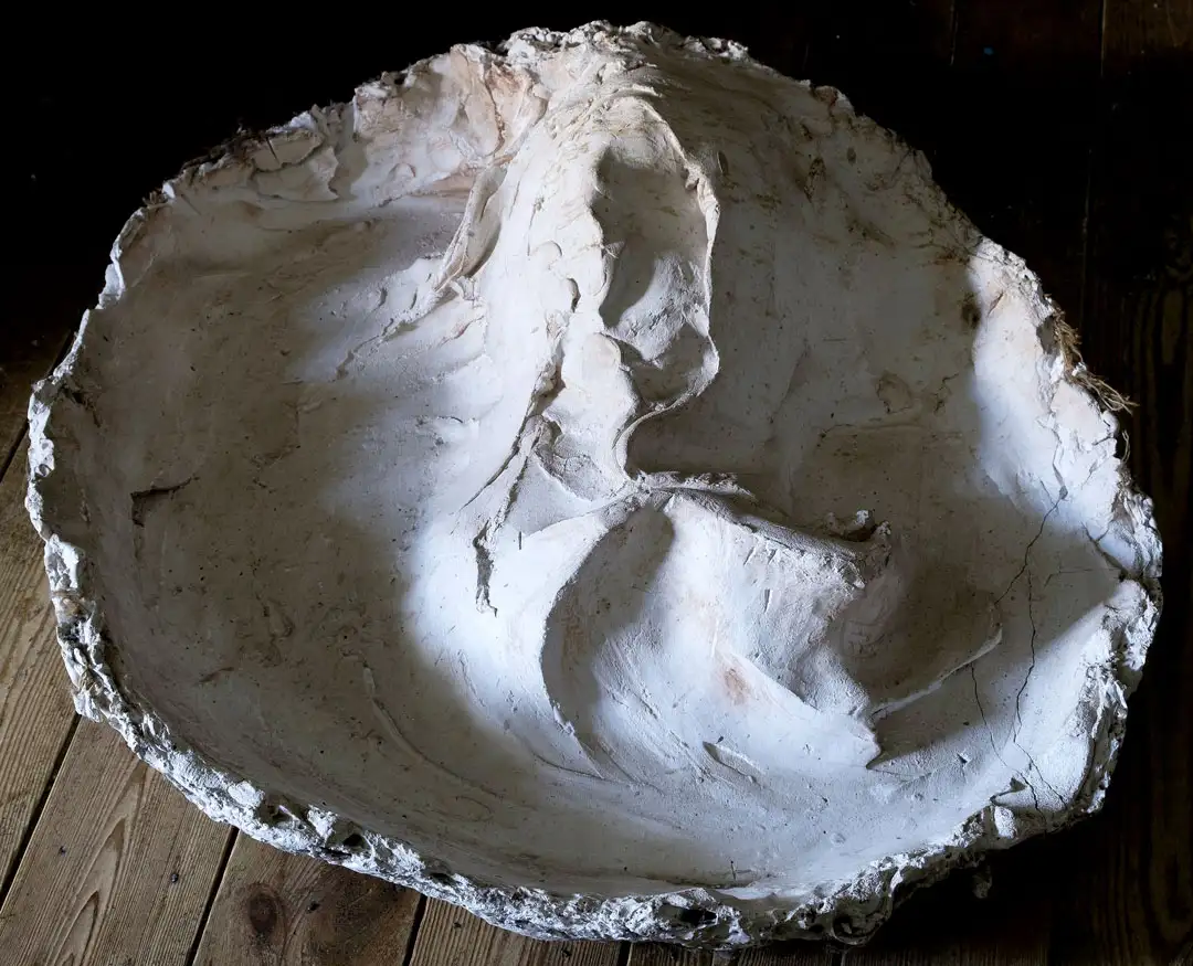 A round plaster sculpture resembling a face within a bowl